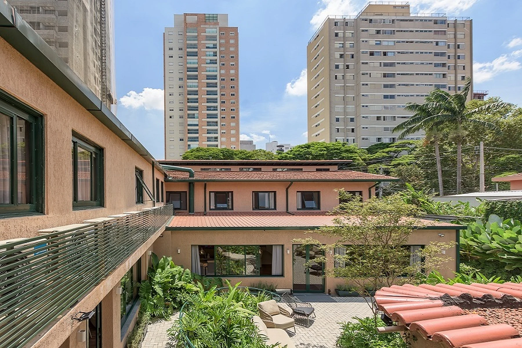 Um ambiente externo ou jardim com mesas e bancos de madeira e vegetação, criando um espaço de lazer ao ar livre."