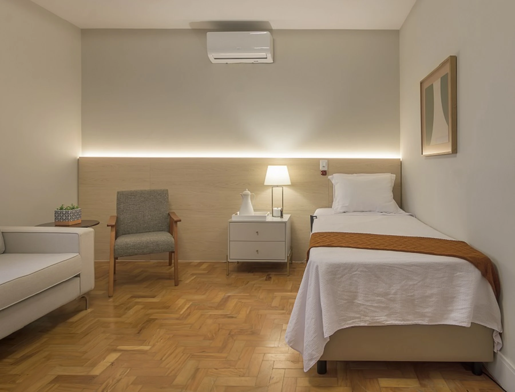 Um quarto de hospital ou de casa de repouso, mostrando uma cama, mesa de cabeceira e decoração simples.